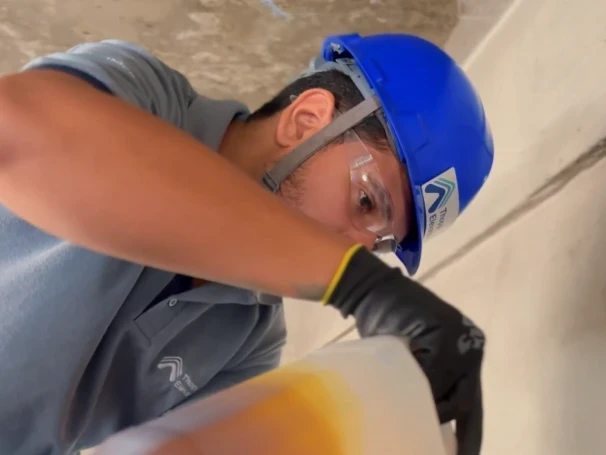 Técnico da Thopp Elevadores, de capacete, óculos e luvas de proteção, repondo o óleo da máquina de tração durante a manutenção preventiva