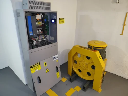 Casa de máquinas modernizada, com quadro de comando novo e máquina de tração com proteção pintada de amarelo