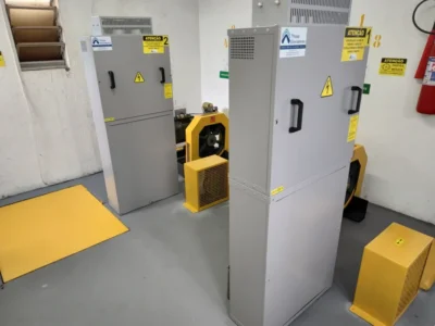 Casa de máquinas com dois quadros de comando novos e máquinas de tração com proteções amarelas