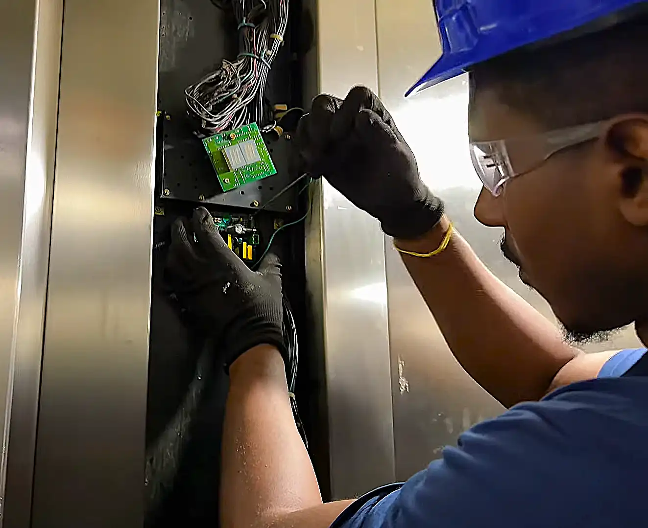 Técnico da Thopp Elevadores, de capacete, luvas e óculos de proteção, trabalhando nas placas da botoeira de um elevador