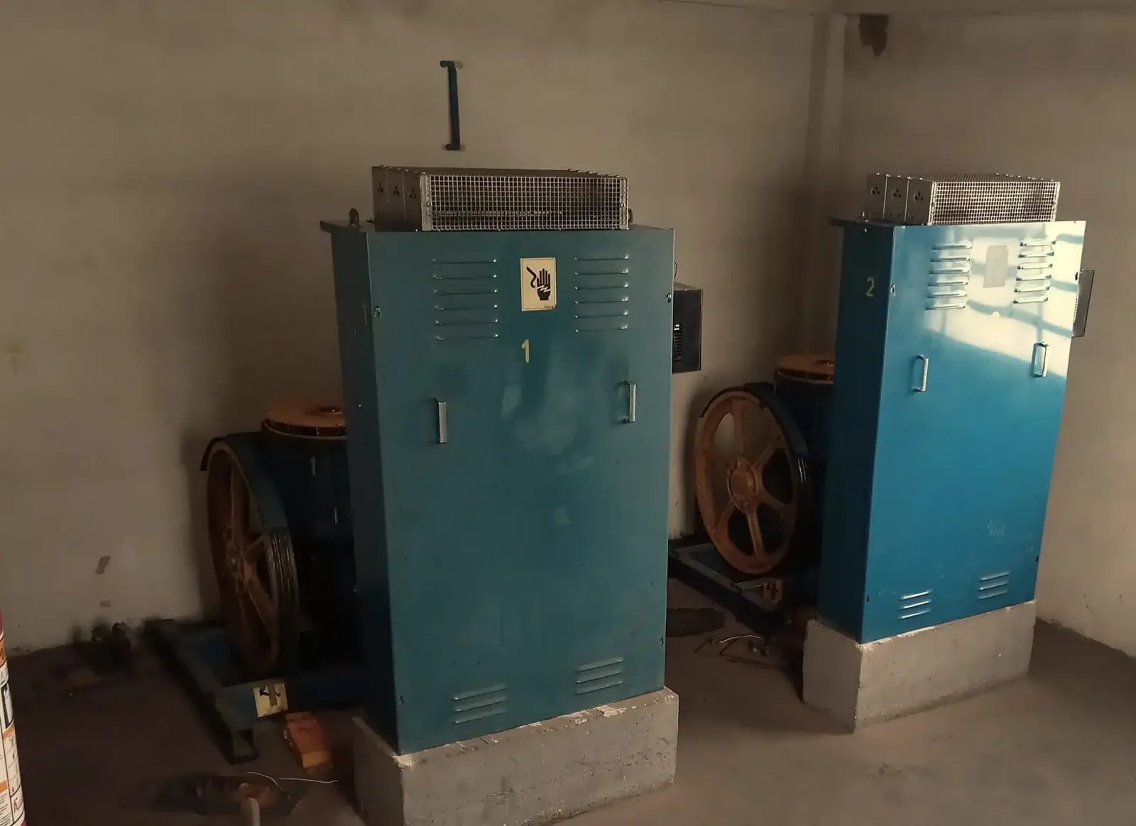 Casa de máquinas antes da modernização, com os dois quadros de comando anteriores, pintados de azul e numerados 1 e 2, ao lado das máquinas de tração