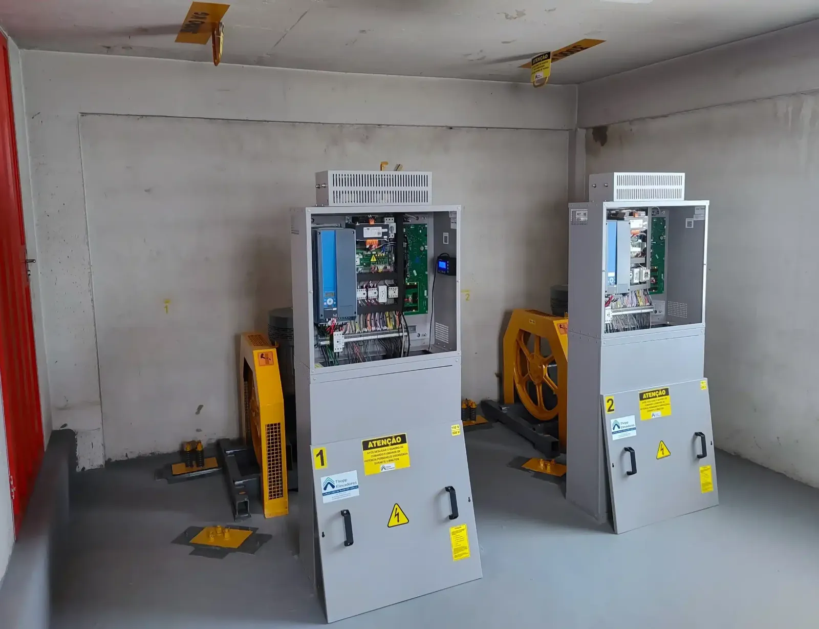 A mesma casa de máquinas depois da modernização, com dois quadros de comando novos da Thopp, sinalização de segurança e proteções amarelas nas máquinas de tração