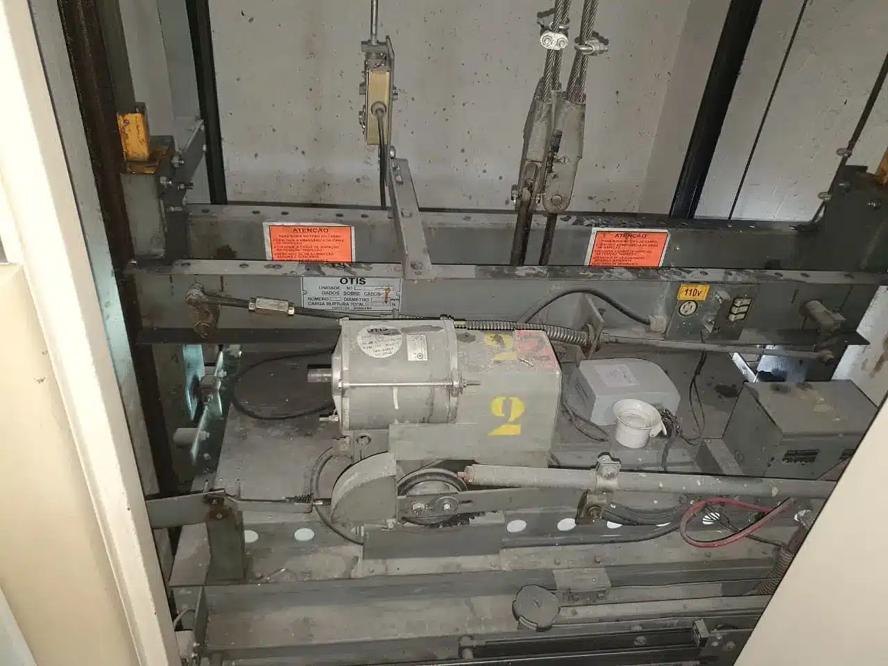 Topo da cabine de um dos elevadores do edifício na Rua Peperi antes da modernização, com o operador de porta anterior, os cabos de tração e a placa de dados na travessa da armação